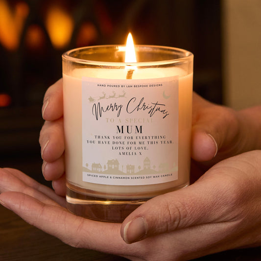 Hand holding a lit candle with a 'Merry Christmas Mum' label against a warm, blurred background.